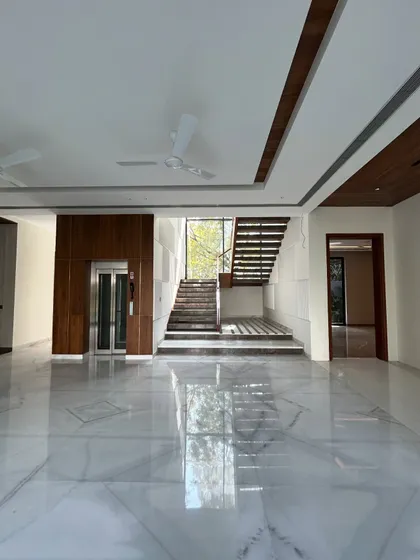 A wide shot of the Gulmohar Farmhouse foyer, showing the relationship between the elevator, staircase, and the expansive, polished marble floor.