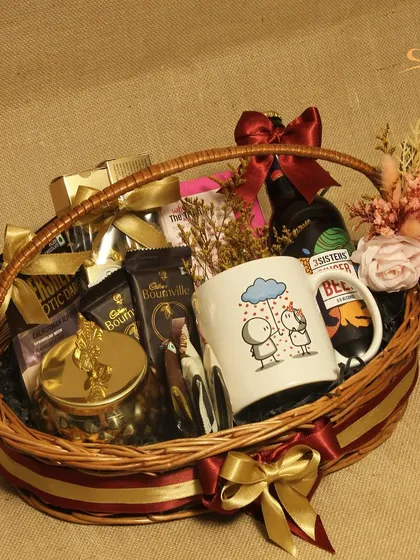 A cozy and comforting hamper in a classic wicker basket. This gift includes a cute illustrated mug, a non-alcoholic beer, and plenty of chocolates and snacks.