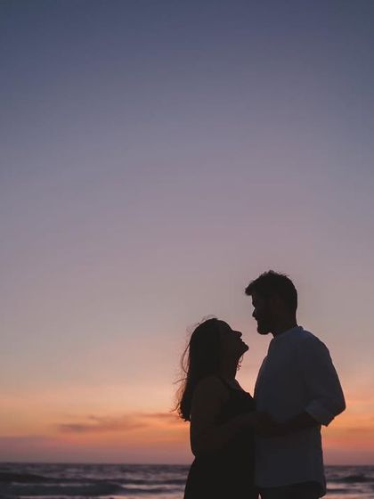 A classic silhouette of a couple against the vibrant colors of a sunset sky over the ocean. These are the timeless, romantic shots that become cherished memories.