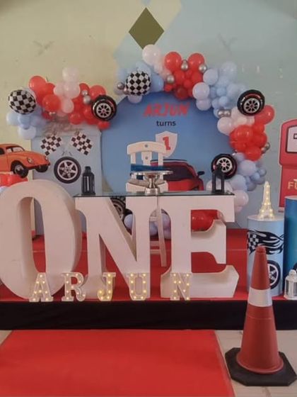 A high-energy 'Cars' movie themed first birthday party. The decoration includes character cutouts like Lightning McQueen, a custom backdrop, and props like traffic cones and tires to create a racetrack feel.