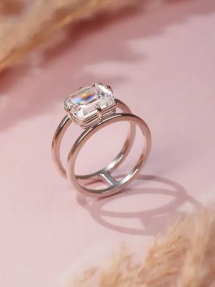 A modern silver ring with a large crystal, shot against a soft pink background with pampas grass. The soft textures and colors create a feminine and sophisticated mood.