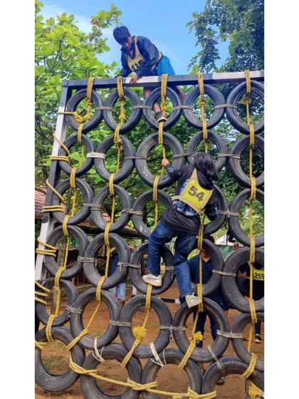 A duplicate of participants tackling a tire wall obstacle. Our leadership camps involve challenging physical activities that build confidence.