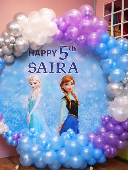 A magical trip to Arendelle with this Frozen-themed party. The backdrop features Elsa and Anna, surrounded by a beautiful balloon arch of icy blues, purples, and silver.