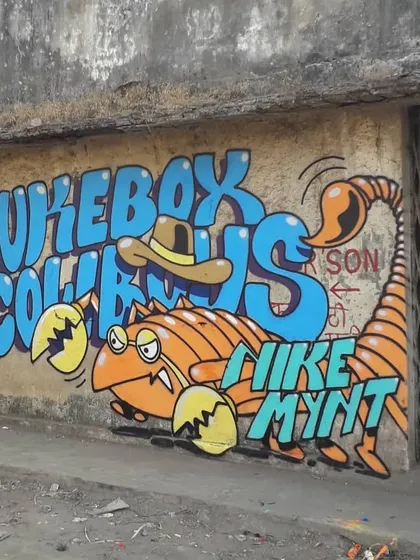 A slightly different angle of the "Jukebox Cowboys" mural, showing more of the surrounding weathered wall and metal gate, which gives context to its urban location in Virar.