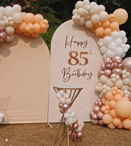 An elegant outdoor decoration for an 85th birthday. I used custom arched backdrops and a beautiful balloon garland in soft pastel and rose gold tones for a sophisticated and celebratory look.
