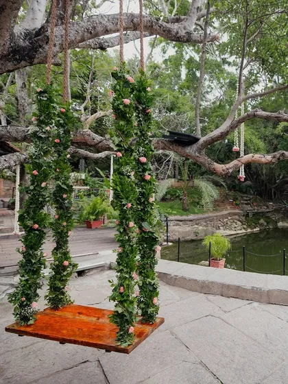 The swing, decorated with greenery and soft pink roses, set against the backdrop of the pond, creates a fairytale-like setting.