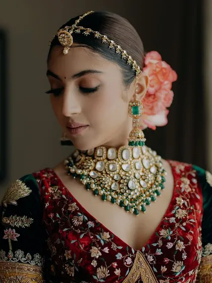 A beautiful close-up of bride Sharun, highlighting her flawless makeup and the stunning emerald and polki jewelry. The flower in her hair adds a touch of softness and romance.