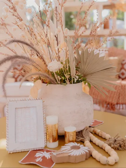 A tabletop centerpiece with a textured vase, dried palm leaves, candles, and a beaded photo frame, adding layers of texture and detail to the decor.