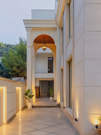 The entrance pathway of the neoclassical home features a grand archway that creates a formal sense of arrival. The warm lighting and clean lines guide the eye towards the main door.
