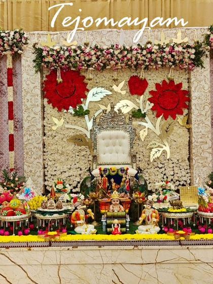 A grand baby shower display with a backdrop of white and red flowers. The intricate arrangement of plates, dolls, and traditional lamps creates a visually stunning and culturally rich celebration.