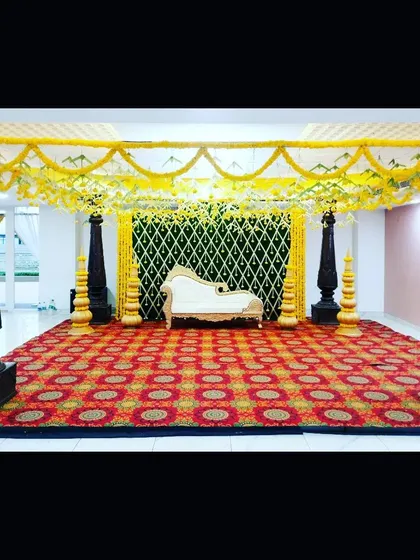 A classic mantap I constructed for a traditional ceremony. The design features four ornate black pillars, a canopy of bright yellow marigold garlands, and a decorative backdrop, all set upon a richly patterned carpet to create a grand and sacred space.
