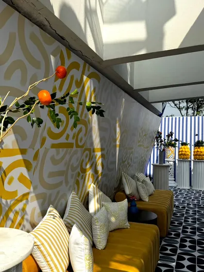 Sunlight streams into the lounge area, highlighting the textures and patterns of our Uttarayan decor. The combination of the abstract wall, striped cushions, and geometric floor creates a vibrant, layered look.