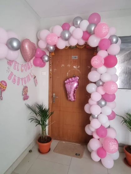 A pink, white, and silver balloon arch framing a doorway to welcome a baby girl home.