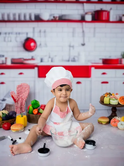 A cheeky grin from our little chef. The red and white kitchen backdrop makes these portraits pop.
