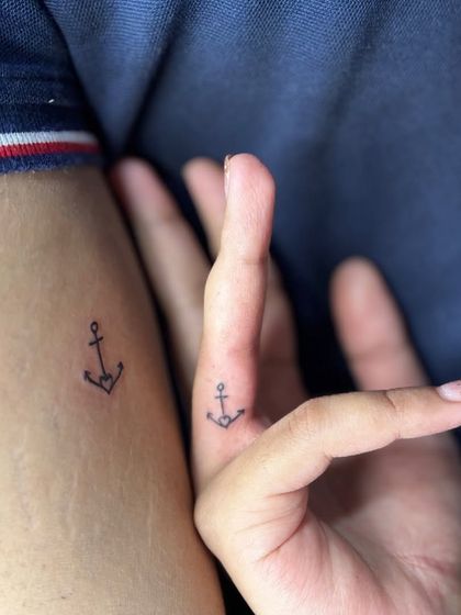 A simple and classic matching tattoo for a couple. A small anchor on the finger and arm symbolizes stability and being grounded in each other.