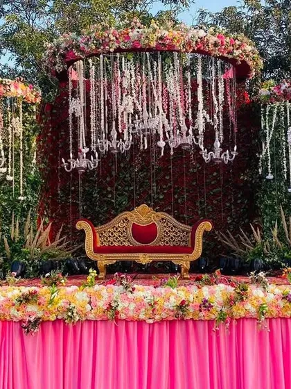 A lush and romantic stage design, with a backdrop of greenery and hanging chandeliers, all framed by a cascade of flowers.