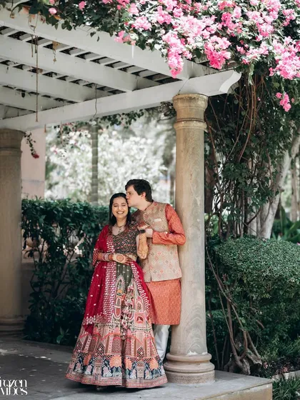 A sweet, romantic moment under a bougainvillea-covered arch. The groom's gentle kiss on the bride's head is a perfect, tender detail.