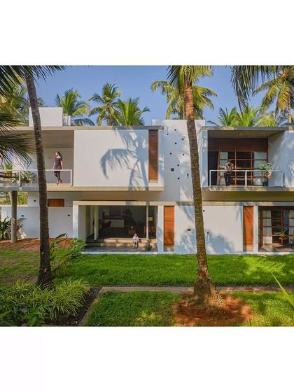 The Aayi House is designed to embrace its tropical setting, with large balconies and openings that connect the living spaces to the lush garden and palm trees.