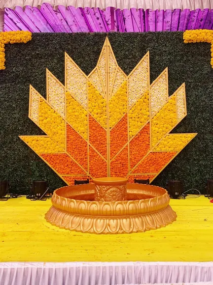 This geometric lotus backdrop for a Haldi ceremony was crafted using petals of yellow and orange marigolds. The design combines modern patterns with the traditional flower of celebration, all centered around a brass urli.