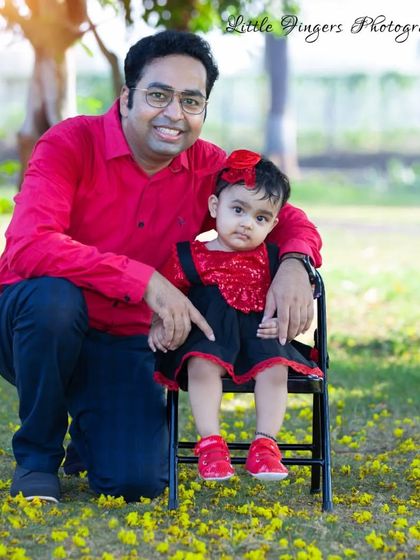 A proud father kneels next to his daughter, who is dressed in a cute red and black outfit. A simple, happy portrait from a one-year-old's birthday shoot.