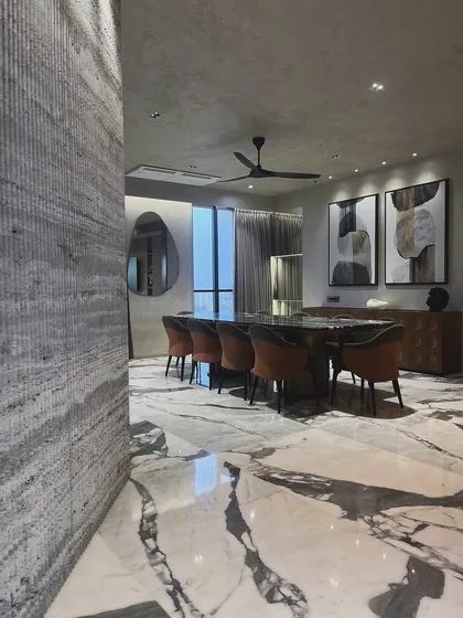 Here, the dining space is anchored by a stunning marble floor with heavy veining, contrasted with a textured travertine wall. This interplay of materials is central to achieving a sense of modern, grounded luxury.