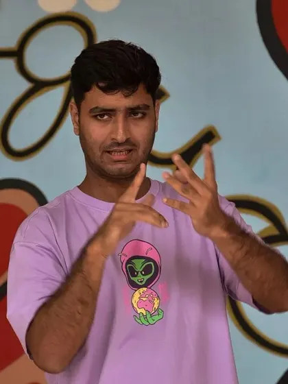 A Deaf instructor passionately explaining a concept in Indian Sign Language against a colorful mural. Our workshops are dynamic, visual, and engaging.