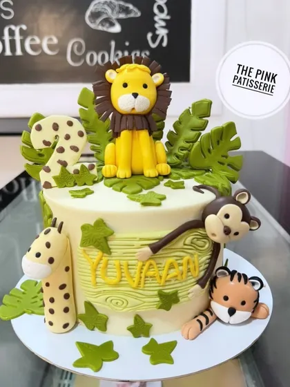 A jungle-themed cake for a second birthday. This design features a lion, giraffe, tiger, and monkey surrounding the cake, with a wood grain texture on the name.
