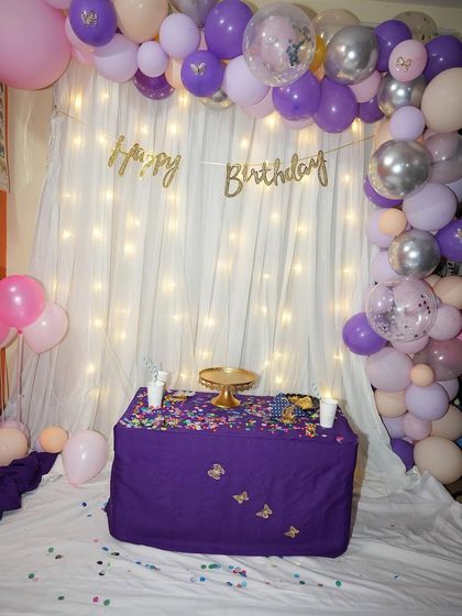 A slightly different view of the purple and pink birthday backdrop. The combination of the soft curtain, twinkling lights, and a colorful balloon garland makes for a simple yet beautiful setting for any celebration.