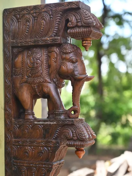 A close-up of the elephant bracket, focusing on the detailed carving of the head and trunk. The wax brown finish gives the wood a warm, natural luster.