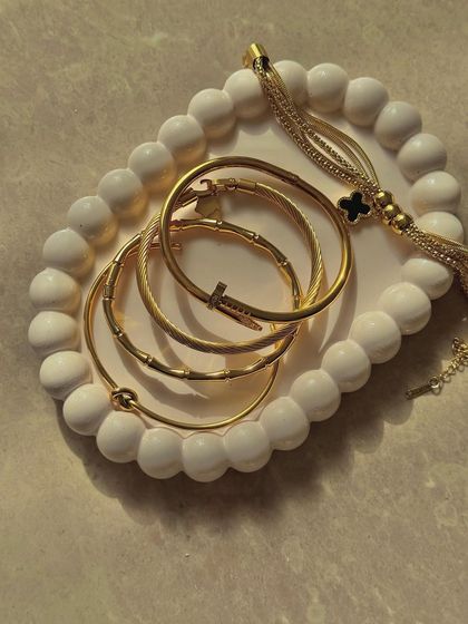 An assortment of gold bangles and bracelets arranged on a textured white tray. The composition and lighting create an interesting and aesthetically pleasing product shot.