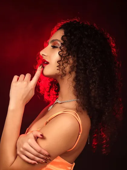 A beauty portrait with a model in an orange dress, lit with a dramatic red backlight that creates a fiery halo effect.