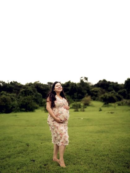 A happy solo portrait of the mom-to-be in a floral dress, standing in a field and cradling her bump with a contented smile.