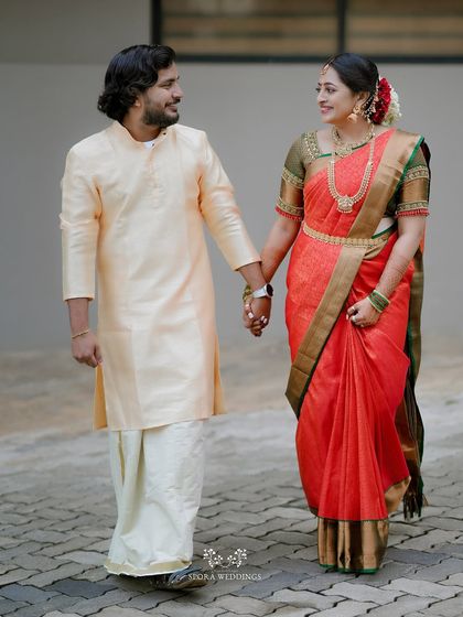A beautiful Kerala couple walking hand-in-hand, the bride in a stunning red and gold saree and the groom in a traditional mundu.