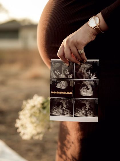 A stunning golden-hour shot focusing on the sonogram pictures held against the baby bump. The warm light creates a magical, glowing effect.