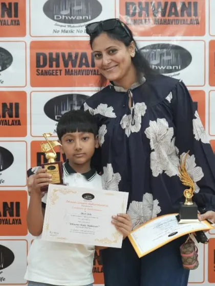 A mother proudly stands with her son, who is holding his awards from the Dhwani Kala Mahotsav. Our prize ceremony is a family affair, celebrating student success together.