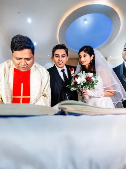 The signing of the register, making it all official. The couple is watched over by their proud fathers, a moment of family unity.