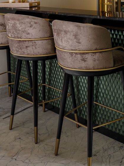A close-up of our custom bar chairs, featuring distressed velvet upholstery and a delicate gold frame. The legs are finished with brass tips, adding a final touch of luxury.