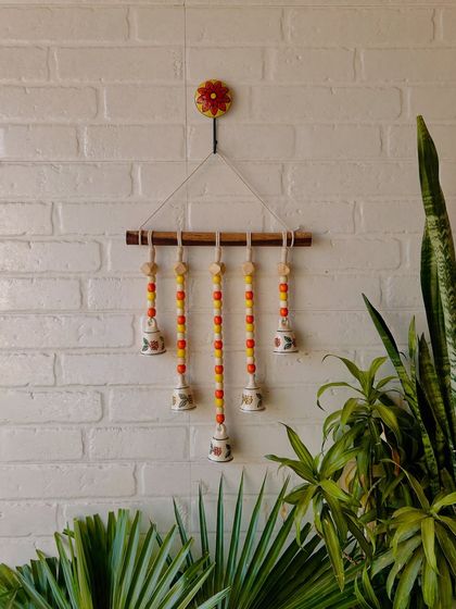 Our 'Beads and Bells' handmade wall hanging, shown here in the 'Sunflower' variant with yellow and orange beads. It comes with a 14-inch dowel and a ceramic wall hook, making it a complete decor piece.