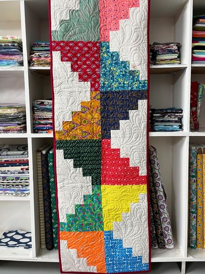 A colorful "log cabin" style table runner or wall hanging, with each block made of contrasting light and dark fabric strips.