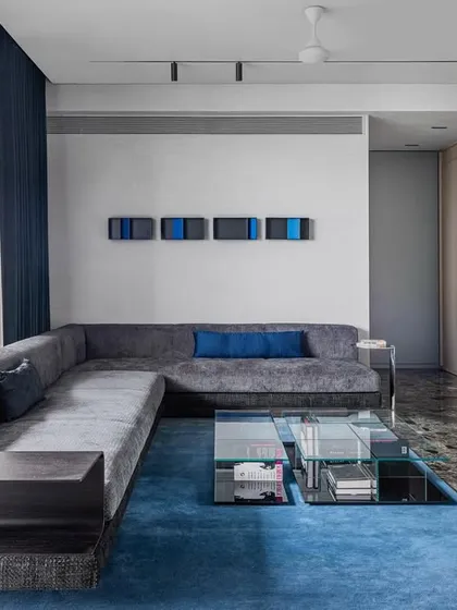 This L-shaped living room was designed to accommodate both formal and informal seating. The space is unified by Ceppo De Gre marble flooring and walls finished in cementitious lime plaster, creating a rich textural foundation. A bold blue rug and matching accents provide a sharp pop of color against the otherwise monochrome and Scandinavian-inspired interior.