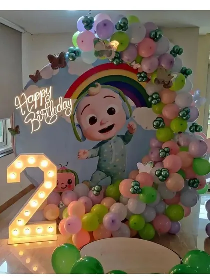 A beautiful circular backdrop featuring the Cocomelon baby, a rainbow, and a 'Happy Birthday' neon sign, framed by pastel balloons.