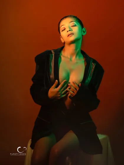 A serene and beautiful pose with eyes closed. The colored light creates a painterly effect on her skin.