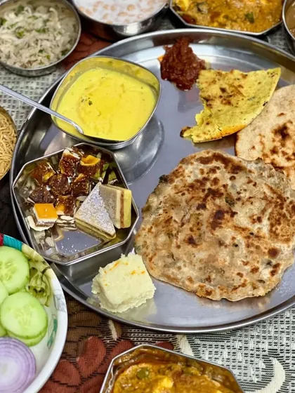 A grand thali featuring a complete meal with paneer sabzi, dal, kadhi, sweets, breads, and salad.