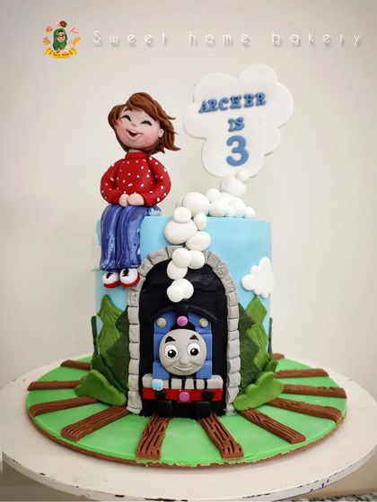 All aboard for a third birthday celebration! This Thomas & Friends themed cake features the iconic blue train emerging from a tunnel. A cute, custom figurine of the birthday boy sits on top, making it a personal and playful tribute to a childhood classic.
