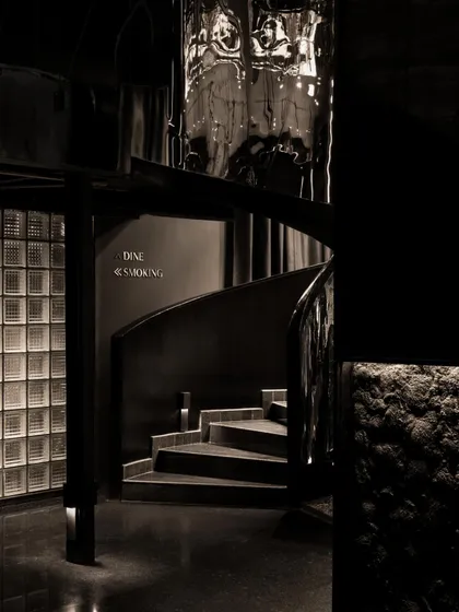 The spiral staircase, a central artery of the space. Its polished, distorted steel surface reflects and abstracts the surroundings, making the ascent or descent a disorienting and memorable part of the journey.