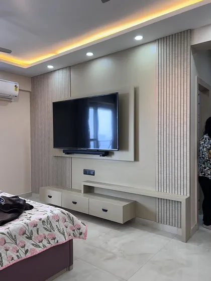 This is a custom-designed TV unit and entertainment center for a bedroom. The design includes fluted wall panels, cove lighting, and a floating console with drawers for a clean, modern look.