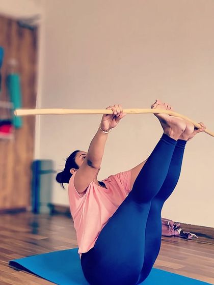 A student engages her core and leg muscles in this challenging seated balance pose, using the stick to assist with leverage and alignment. It's a great way to build strength and focus.