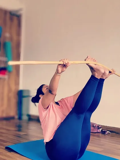 A student engages her core and leg muscles in this challenging seated balance pose, using the stick to assist with leverage and alignment. It's a great way to build strength and focus.
