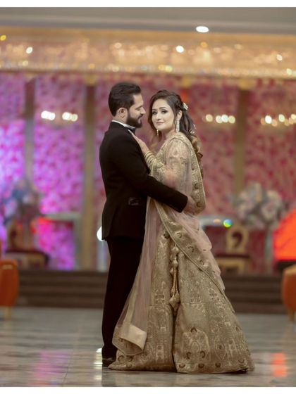 A classic, full-length portrait of the couple in a grand banquet hall. Their pose is elegant and timeless, showcasing their beautiful attire and the opulent setting.