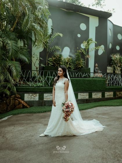 A wide shot of the bride in a modern garden setting, showcasing the full splendor of her wedding dress and long veil.